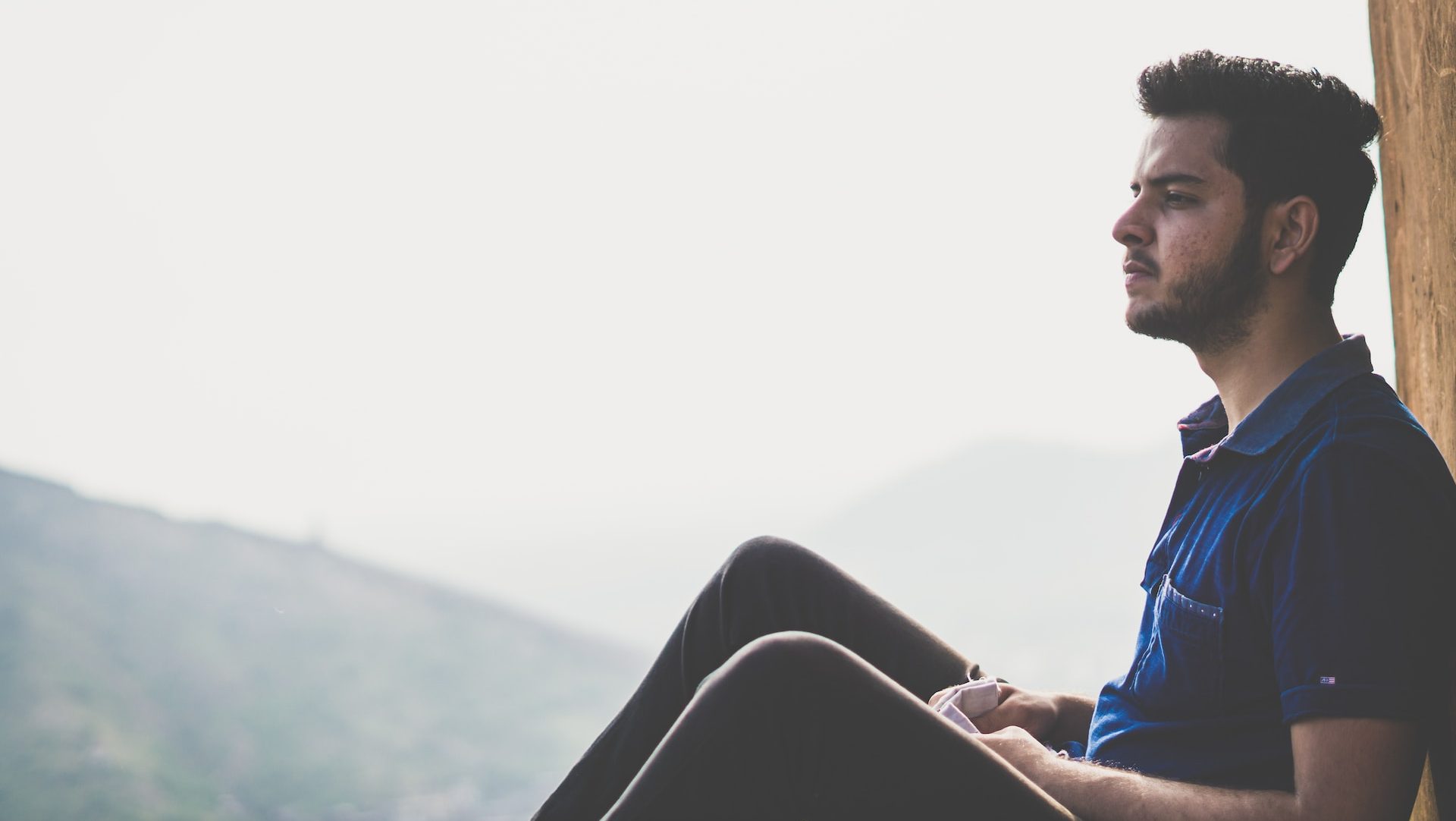 a man sitting on a ledge with a mountain in the background